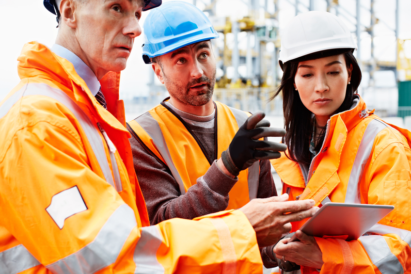 Shot of three workers talking together over a digital tablet while standing on a commercial dock